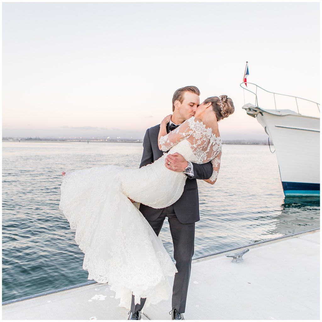 couple kissing, guy holding the bride by the bay with a boat in the background