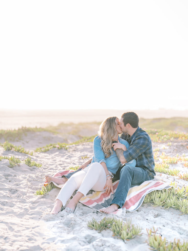 couple sitting cuddling and kissing on the dune on the beach in Coronado, San diego