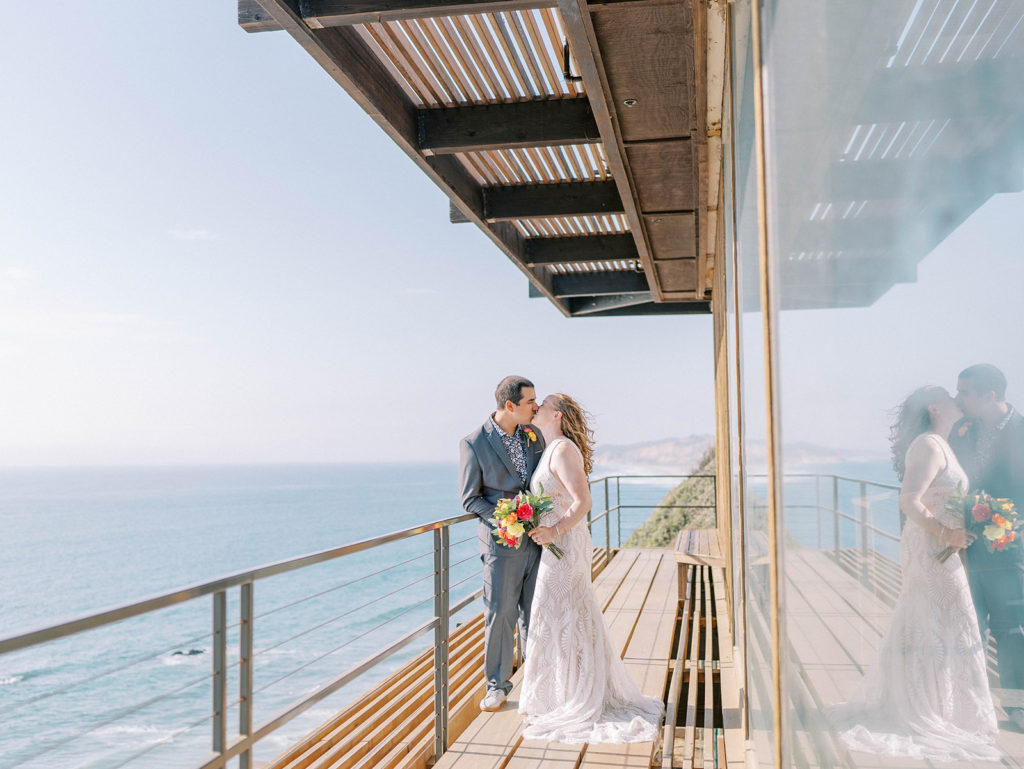 bride and groom kissing after their wedding at the Martin Johnson house with the ocean view in the background