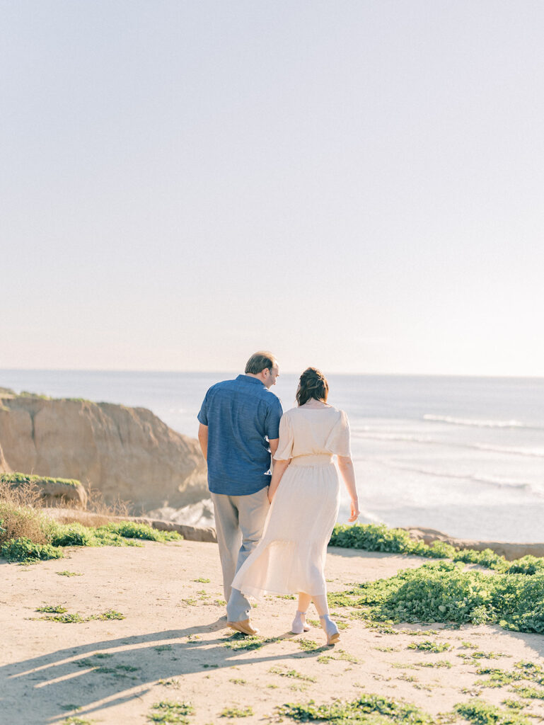 Couple walking and holding hands by the cliffs in sunset cliffs overlooking the ocean