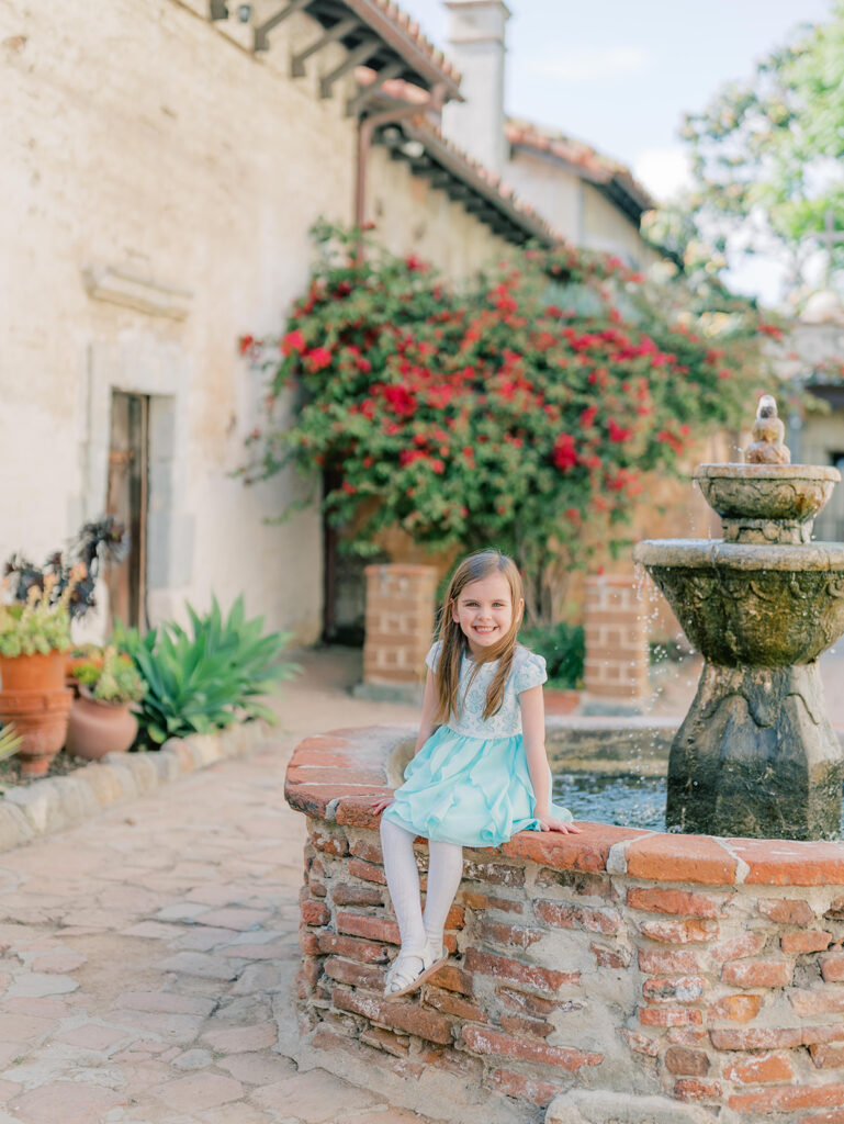 little girl at mission San Juan sitting by a fountain and smiling