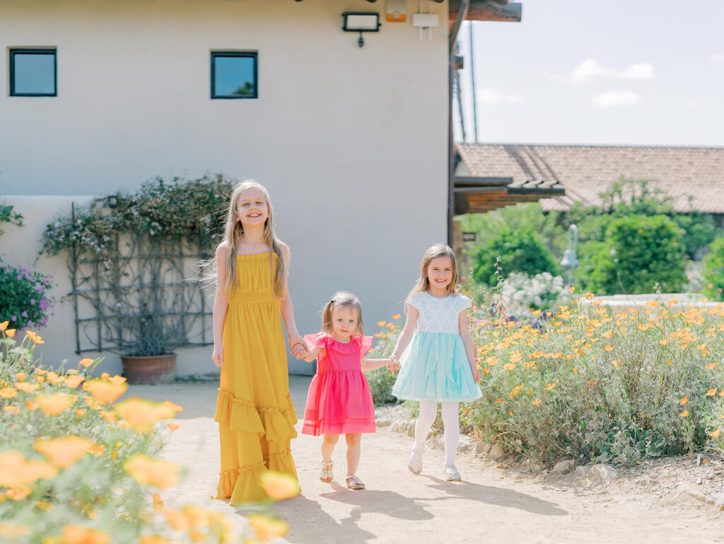 three little girls walking and holding hands through the garden at the mission san Juan Capistrano