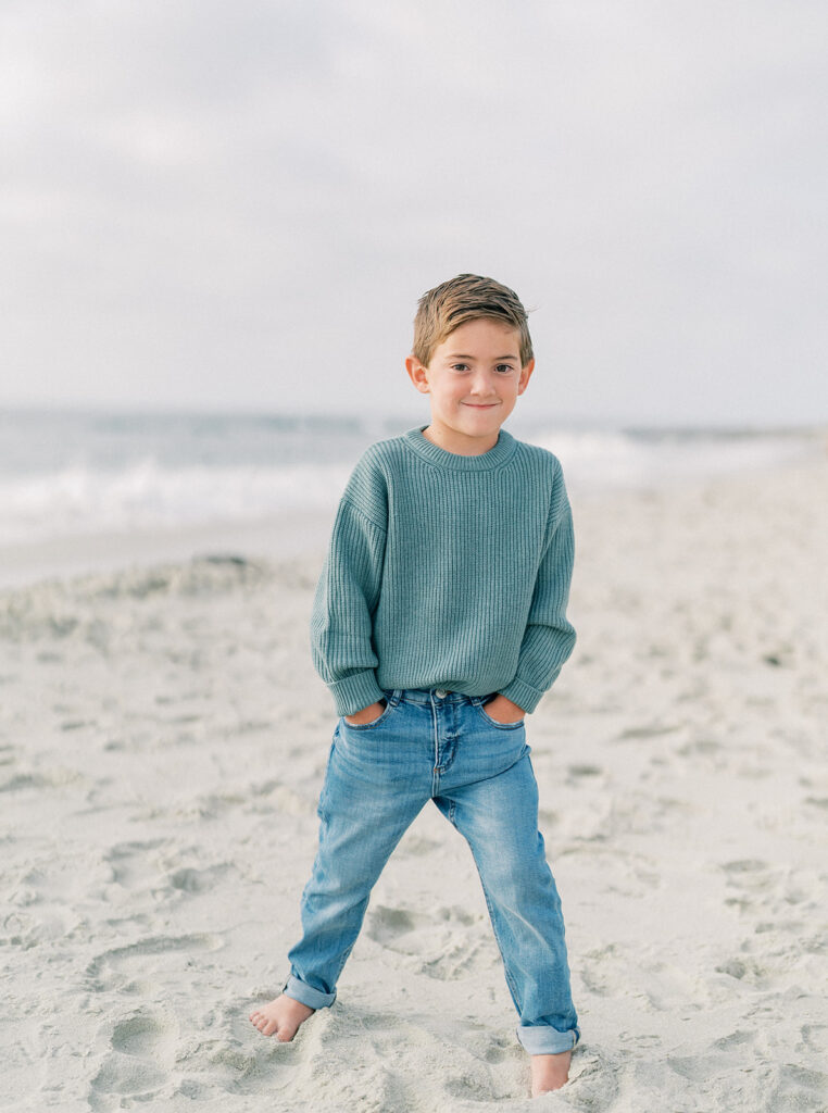 Little boy smiling brightly with the ocean waves and clear sky behind him.