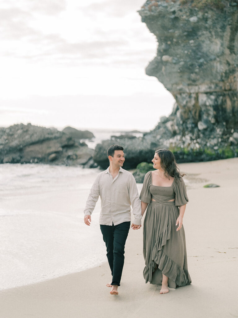 A couple walking hand in hand at Laguna Beach during engagement session