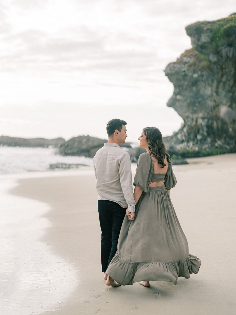 A couple walking hand in hand at Laguna Beach during engagement session