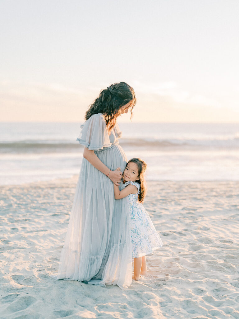 A kid hugging her pregnant mother's tummy captured by San Diego maternity photographer