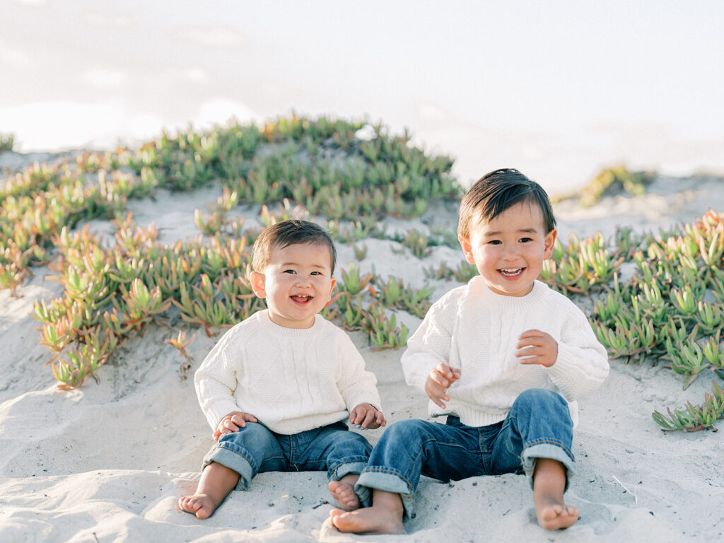 two toddlers sitting side by side on a sandy coronado beach in san diego