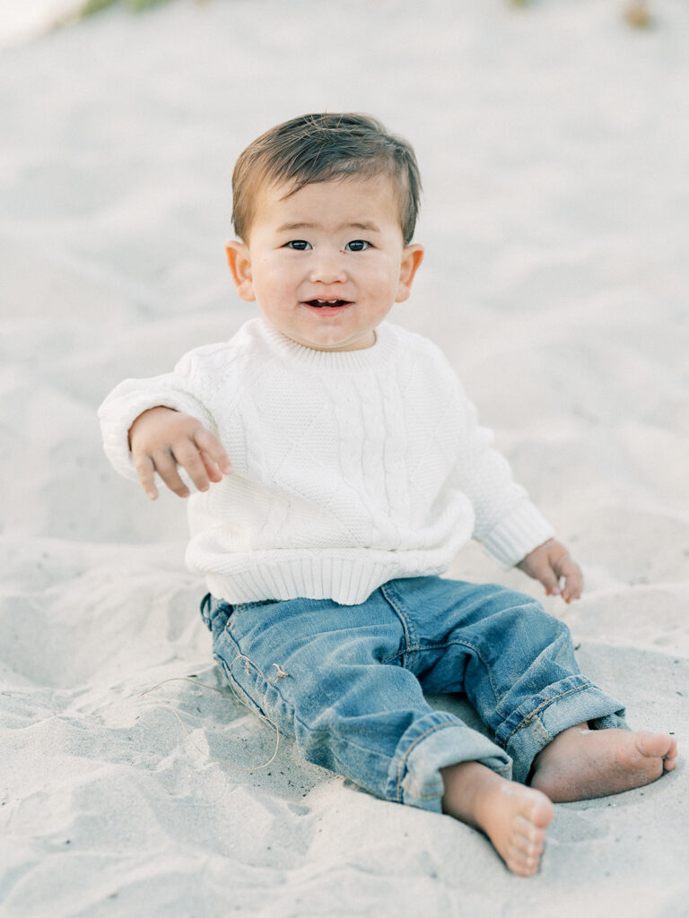 a toddler sitting on a sand while smiling