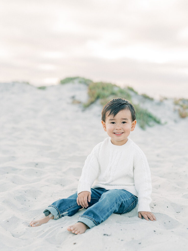 a toddler sitting on a sand while smiling