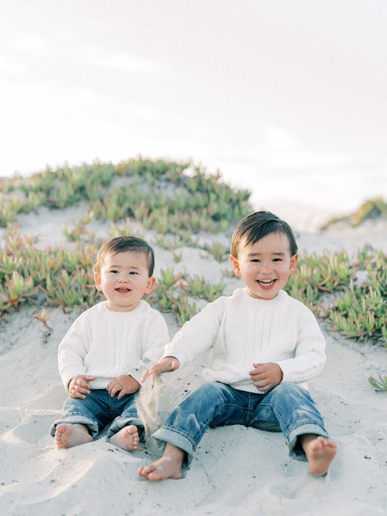 two toddlers sitting side by side on a sandy coronado beach in san diego