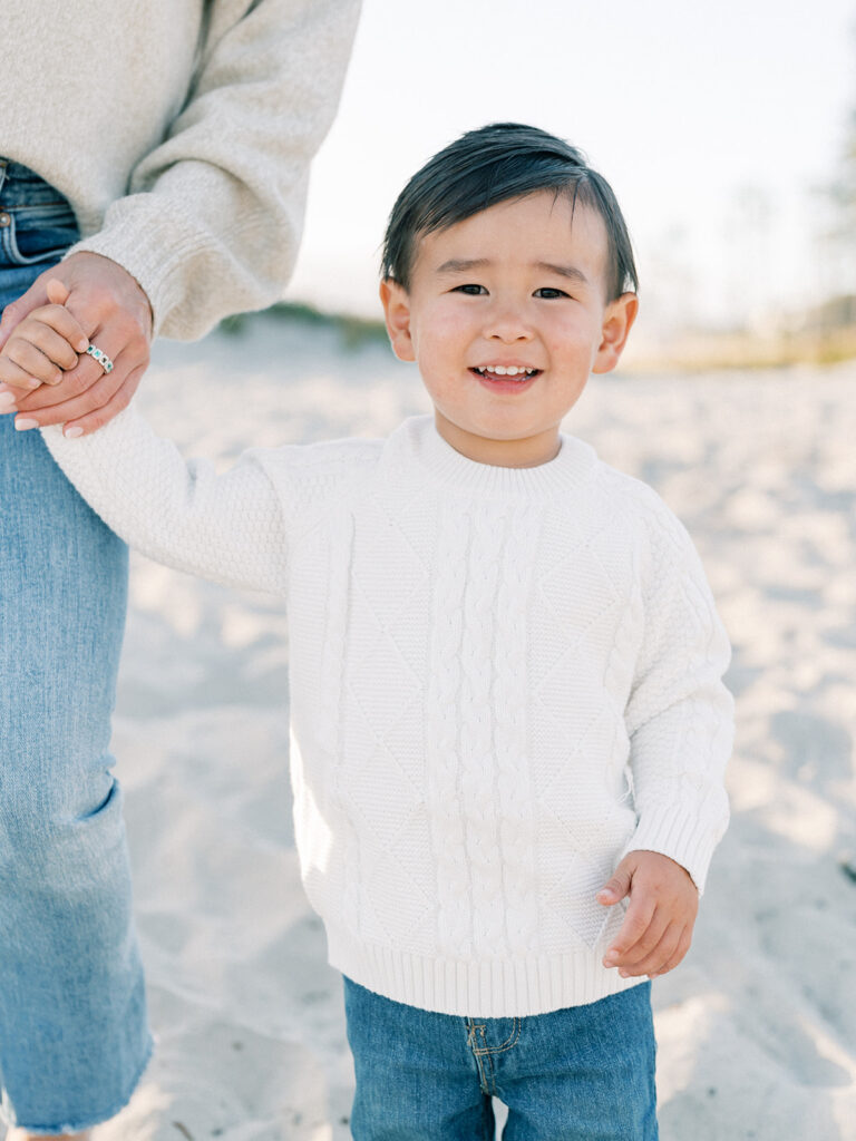 a toddler wearing white sweater while holding her mom's hand