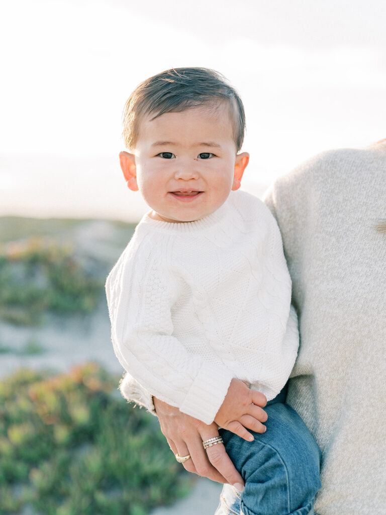 a toddler smiling at the camera while his mother is carrying her