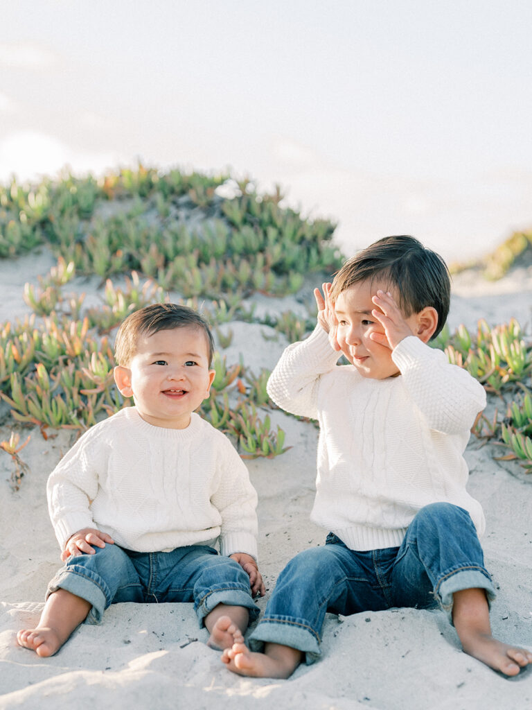 two toddlers sitting side by side on a sandy coronado beach in san diego