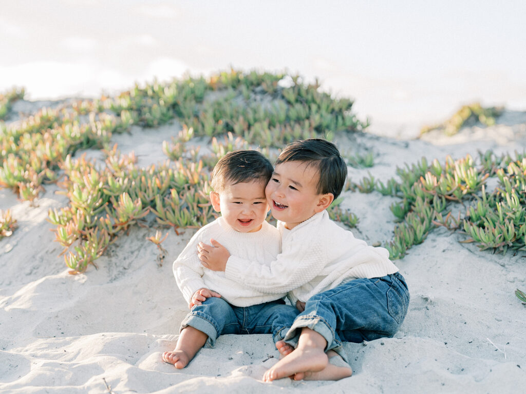 two toddlers sitting side by side on a sandy coronado beach in san diego