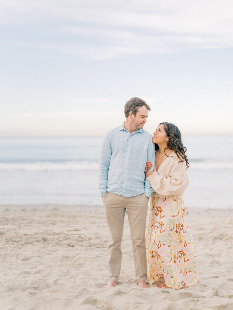 a couple standing in front of pacific beach while straring lovingly at each other