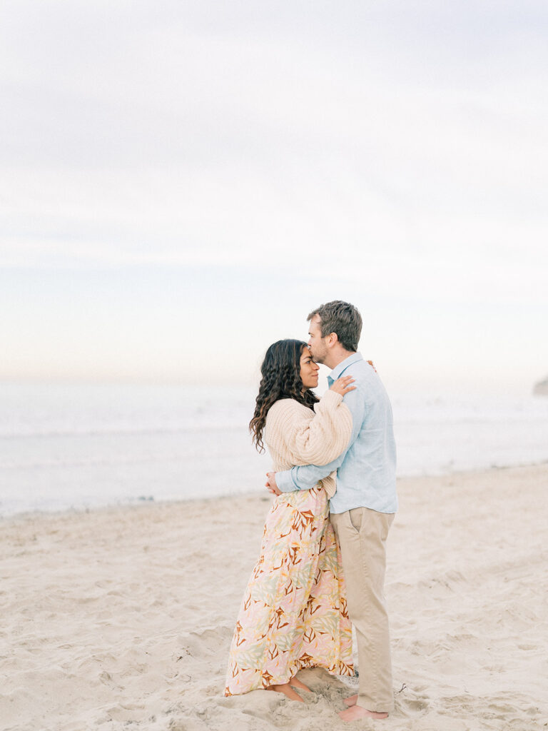 a man kissing her woma's forehead during their engagement session at pacific beach